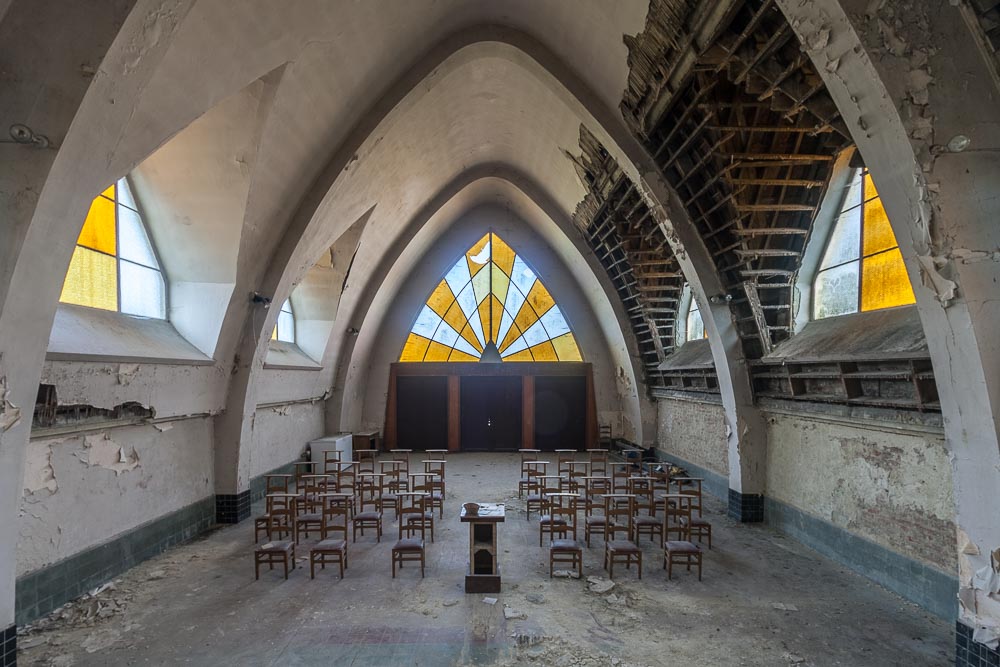binnenzicht in urbex locatie chapelle des mineurs, van altaar
            naar deur en glaspartij
